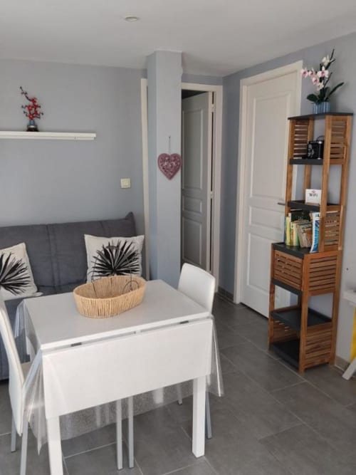Modern open-plan living area at La Pause Landaise with dining table, gray sofa, wooden storage unit, and kitchen facilities