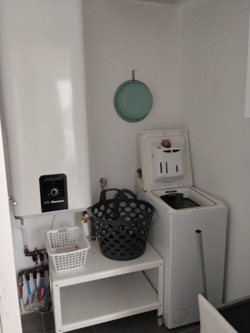 Utility corner in Le Petit Baigneur room at La Pause Landaise showing laundry basket, shelving with baskets, and appliances