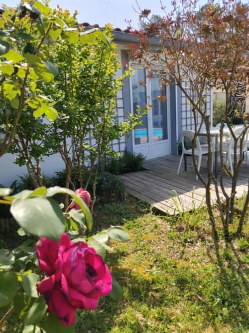 Vibrant pink roses and garden plants frame the terrace entrance to Le Petit Baigneur at La Pause Landaise, a charming Magescq