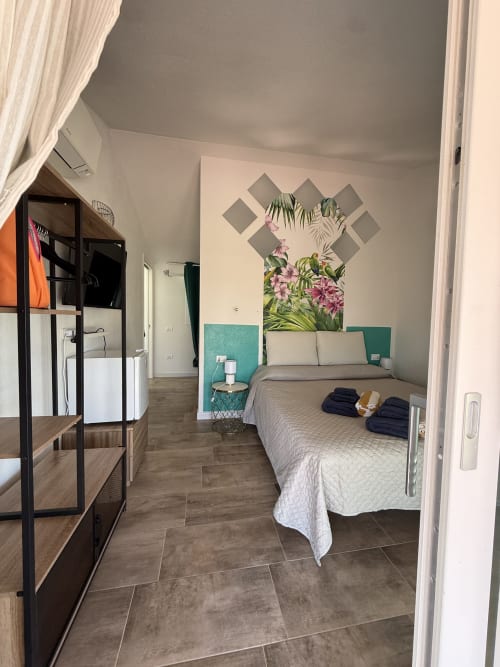 Tropical Room at Sardinia Holidays B&B in Torpè - Queen bed with turquoise headboard, floral wall art, and modern furnishings