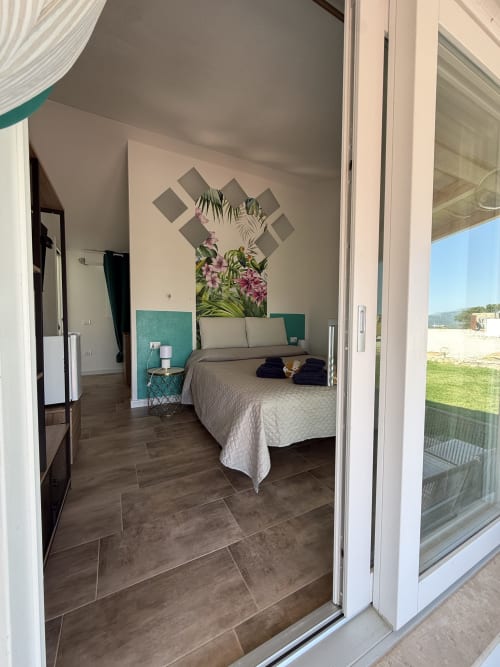 Tropical Room bedroom at Sardinia Holidays B&B in Torpè with ocean view, queen bed, and floral wall art