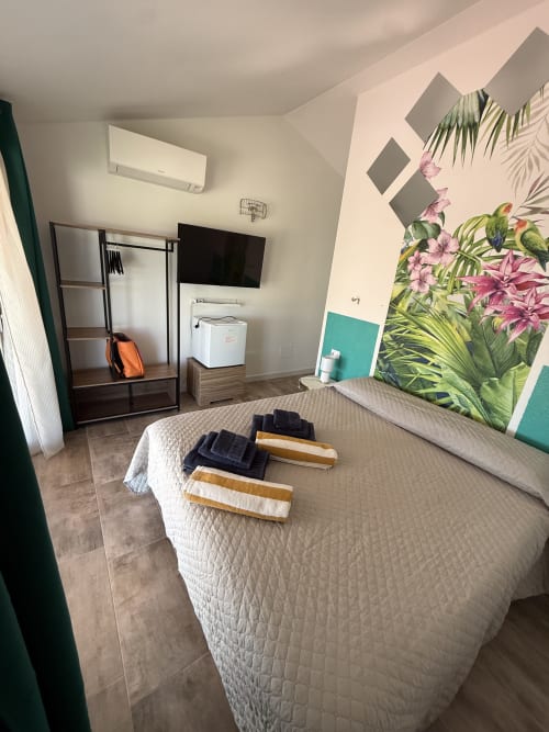 Tropical Room at Sardinia Holidays Torpè with queen bed, AC unit, flat-screen TV, and botanical wall mural