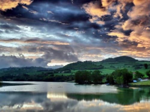 Paesaggio lacustre affascinante presso Villa Andreina ad Amandola con colline ondulate, cielo drammatico e riflessi tranquilli sull'acqua.
