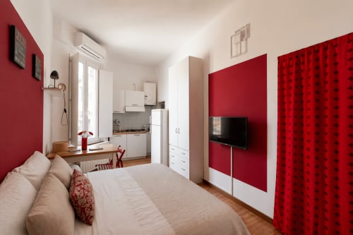 Modern studio apartment in Milano's Navigli district with red accent walls, kitchenette, flat-screen TV, and comfortable bed