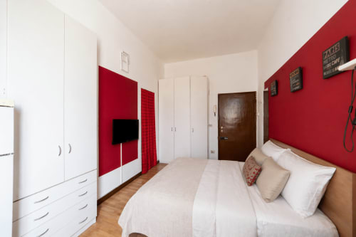 Modern bedroom at HB Hall Navigli apartment in Milano with red accent wall, queen bed, flat-screen TV, white wardrobes, and