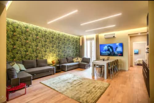 Modern Roma apartment living room with green accent wall, gray sofa, flat-screen TV, wooden floors, and contemporary