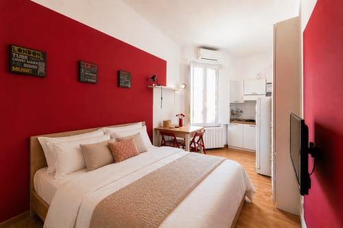 Modern Milano studio with red accent wall, wooden bed, kitchenette, and wooden flooring at HB Hall Hotel