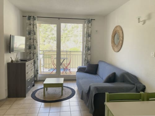 Salon d'appartement moderne avec canapé bleu, vue montagne sur balcon, télévision et mobilier contemporain chez LOCADIGNE