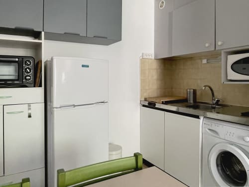 Cuisine moderne de LOCADIGNE avec électroménagers blancs, cuisinière, lave-linge et dosseret en carrelage beige