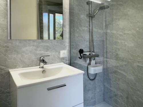 Salle de bain moderne du studio LOCADIGNE avec vasque blanche, carrelage gris, douche et fenêtre vue montagne