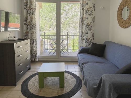 Salon moderne avec canapé bleu, balcon vue montagne, mobilier bois et tapis rond chez Locadigne