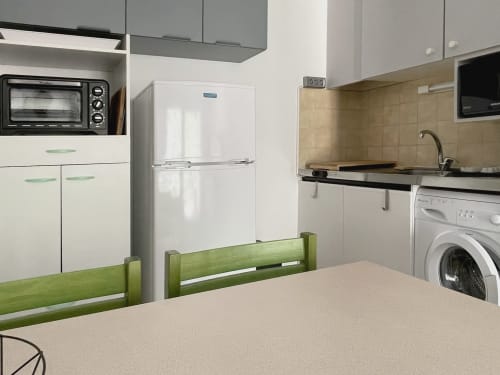 Cuisine moderne de l'appartement LOCADIGNE avec placards blancs, réfrigérateur, lave-linge, cuisinière et table à manger verte