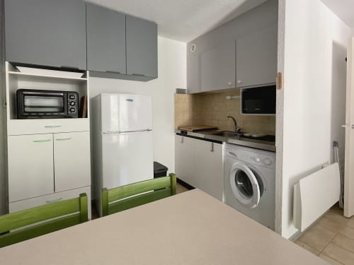 Cuisine-buanderie moderne de l'appartement LOCADIGNE avec armoires grises, réfrigérateur blanc, cuisinière, lave-linge et salle à manger verte