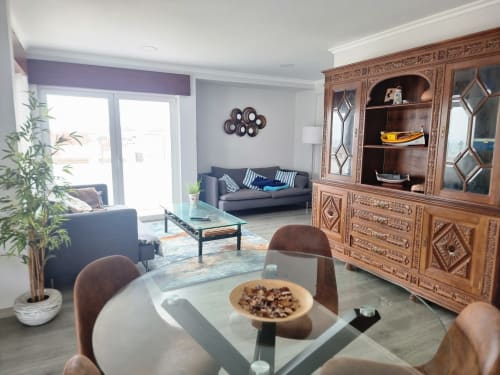 Sala de estar moderna na Casa da Barroca, Ericeira com mesa de jantar, sofá, móvel em madeira trabalhada e vista para a cidade