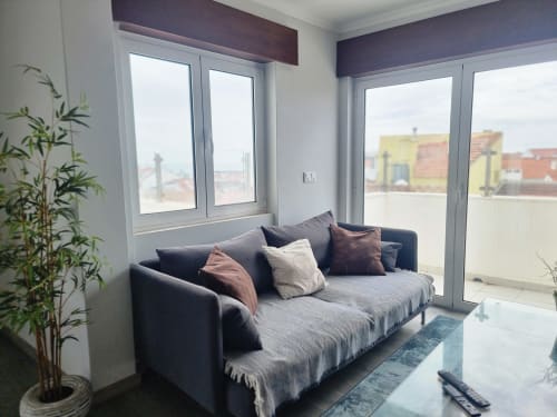 Sala de estar moderna com sofá cinzento, vista para a cidade e planta em vaso na Casa da Barroca, Ericeira