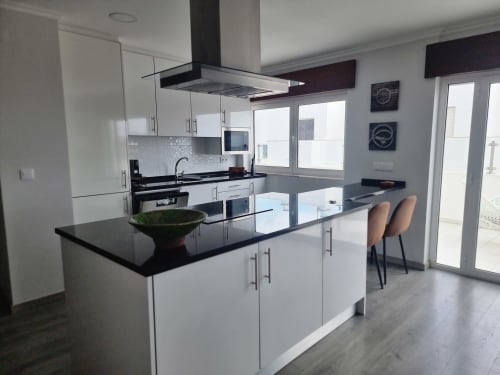 Cozinha moderna da Casa da Barroca em Ericeira com armários brancos, bancadas pretas, balcão com assentos e portas de vidro