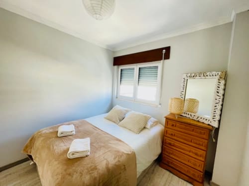 Quarto aconchegante da Casa da Barroca em Ericeira com cama de casal, cômoda de madeira e janela com vista para a cidade