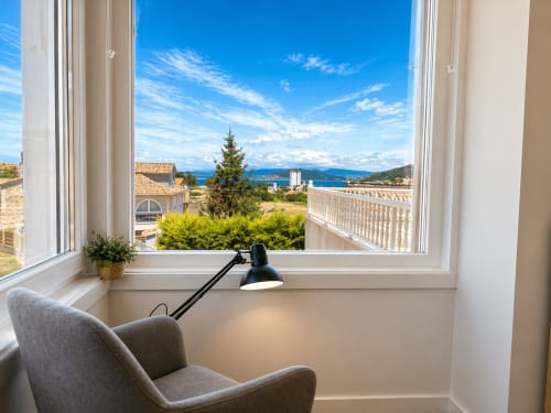 Apartamento en Baiona con vistas panorámicas al mar y montañas, amplio ventanal, sillón gris, lámpara negra y ambiente costero