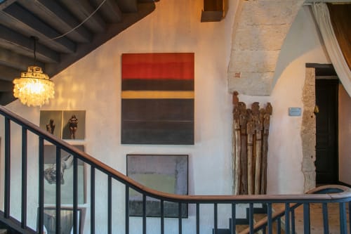 Alombre BnB stairwell in Lectoure features modern art, crystal chandelier, and rustic wooden sculptures on white walls.