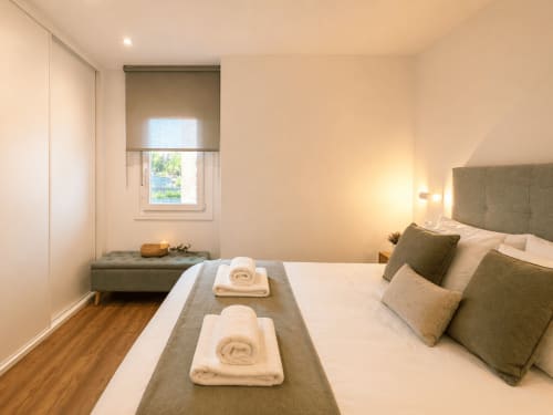 Dormitorio moderno del apartamento Portaliña en Baiona con vistas al mar, cama queen, toallas enrolladas, asiento junto a la ventana y pisos de madera