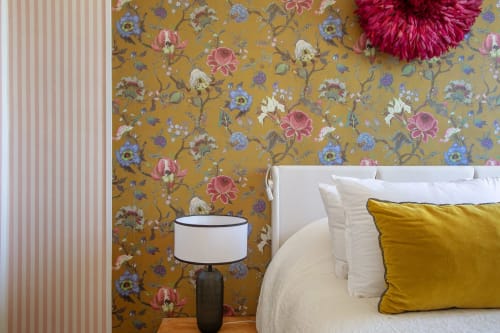 Chambre de la maison d'hôtes Alombre avec papier peint à motifs floraux dorés, lit blanc et coussin moutarde à Lectoure