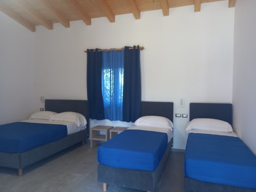 Spacious quadruple room at Agriturismo Lumia Resort with four beds, blue bedding, wooden ceiling beams, and mountain view