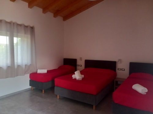 Spacious quad room at Agriturismo Lumia Resort with three red beds, wooden ceiling, and mountain views in Riposto, Sicily