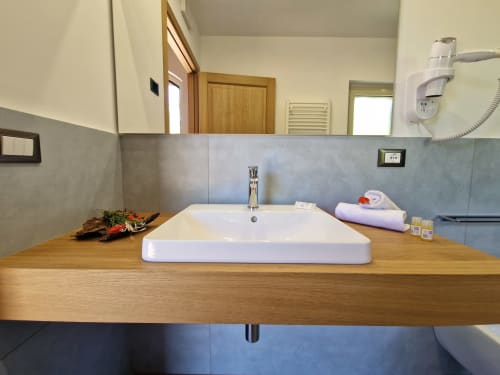 Modern bathroom vanity with wooden countertop, white rectangular sink, and blue-gray tile backsplash at Agriturismo Lumia