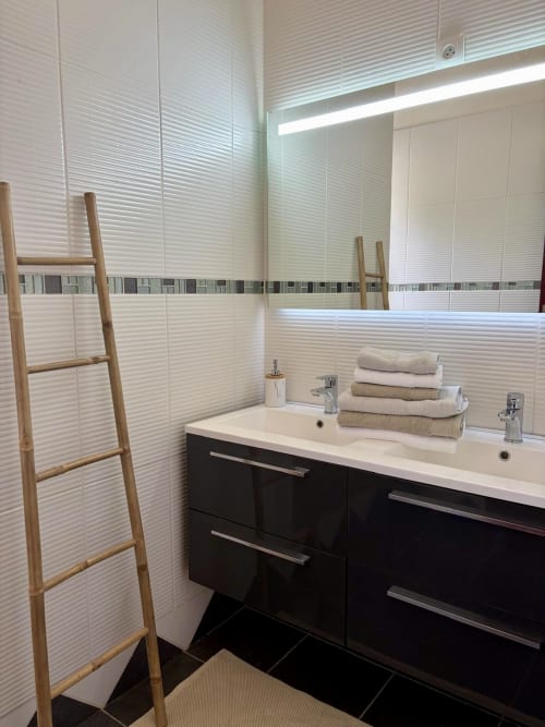 Salle de bains moderne à la villa LÉZILÉ CONCIERGERIE à Bouillante avec double vasque, vanité noire, carrelage blanc texturé et bois