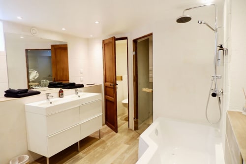 Salle de bains moderne à la Bastide Aïna à Grasse : meuble vasque blanc, douche effet pluie et portes en bois dans cette suite familiale.
