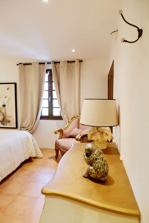 Suite chambre élégante à la Bastide Aïna à Grasse avec décor crème, fauteuil orné, sculpture léopard doré et fenêtre avec