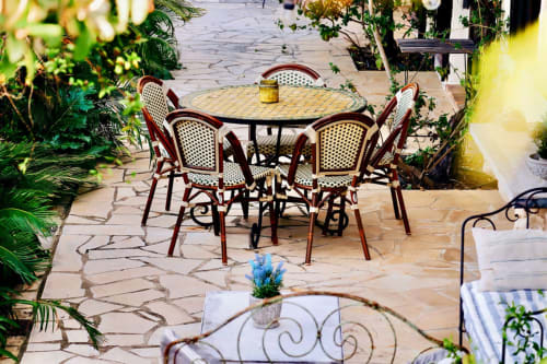 Terrasse luxuriante à la Bastide Aïna à Grasse avec table ronde, chaises en rotin et plantes fleuries.