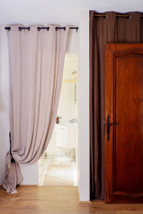 Entrée de salle de bain avec rideau de chambre d'hôte mauve clair et porte d'armoire en bois à la Bastide Aïna à Grasse