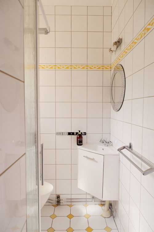 Salle de bains moderne à Bastide Aïna avec carrelage blanc, frise jaune, meuble vasque et miroir rond à Grasse