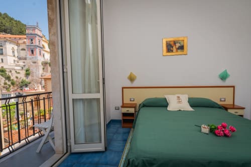 Camera luminosa a Casa Mannini B&B a Maiori con letto verde, balcone con vista sull'architettura storica e vedute costiere