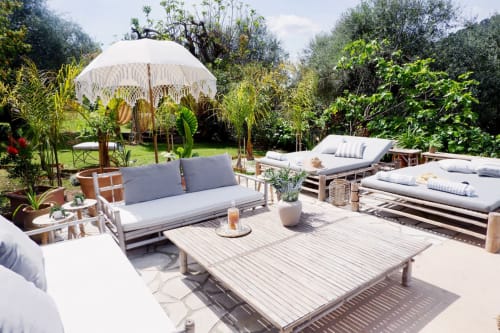 Terrasse du jardin Bastide Aïna à Grasse avec transats, canapé, table de repas, parasol blanc et verdure luxuriante
