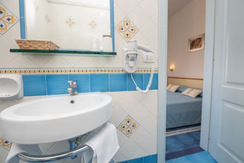 Bagno luminoso con piastrelle blu e motivi decorativi presso la Casa Mannini B&B a Maiori, con lavabo rotondo e accesso alla camera da letto