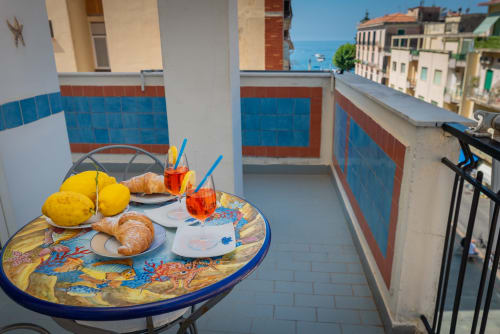 Balcone soleggiato di Casa Mannini a Maiori con tavolo per la colazione, limoni, cornetti e viste sulla costa