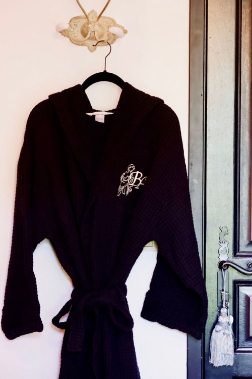 Robe en velours noir avec monogramme brodé suspendue à un crochet décoratif à l'hôtel de charme Bastide Aïna à Grasse, France