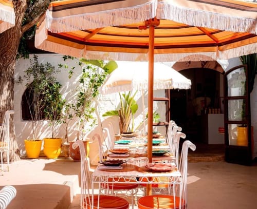 Patio à manger du Riad Eucalyptus avec parasol orange, chaises blanches, table dressée et jardinières jaunes à El Ghazouane