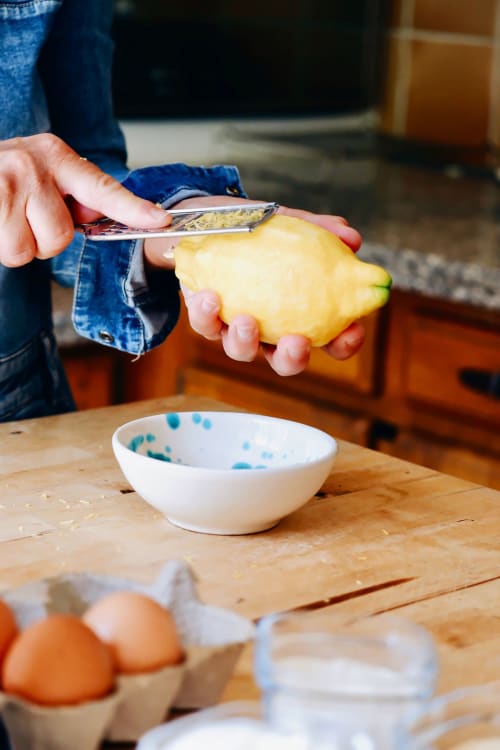 Personne râpant du citron frais à la table de la cuisine de Bastide Aïna à Grasse, avec des œufs et un bol à proximité