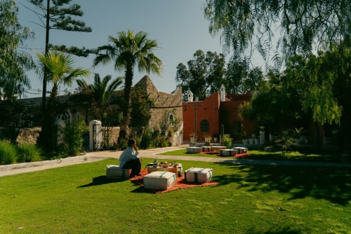 Client se détendant sur le gazon du Riad Eucalyptus, hôtel ethnique à El Ghazouane, Maroc, avec bâtiment rouge traditionnel et palmier