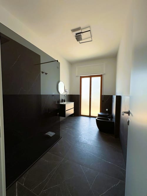 Bagno moderno dell'Hotel Newhouse Bari con piastrelle in marmo nero, doccia in vetro, lavabo sospeso e porte in legno