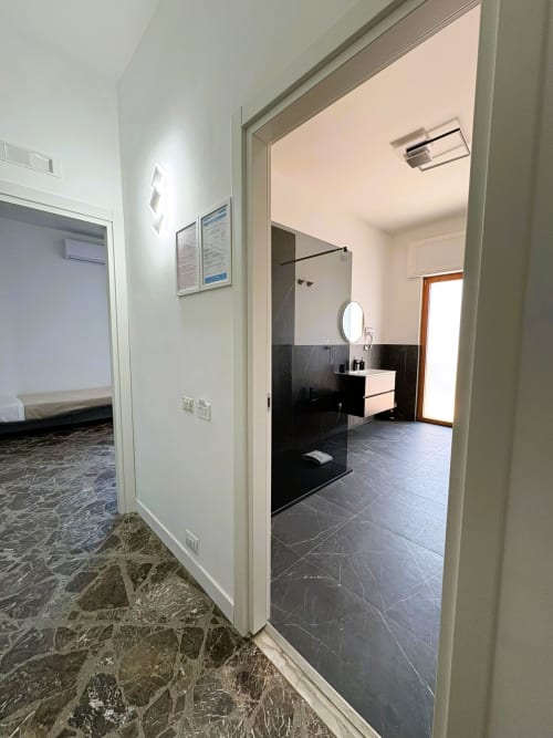Bagno moderno della camera Cavour Deluxe presso l'hotel Newhouse Bari, con pavimento in marmo nero, doccia walk-in e finiture bianche