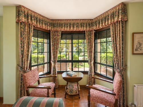 Elegante sala con mirador en la villa As Landras de Galicia con vistas al río, muebles de época y cortinas florales decorativas