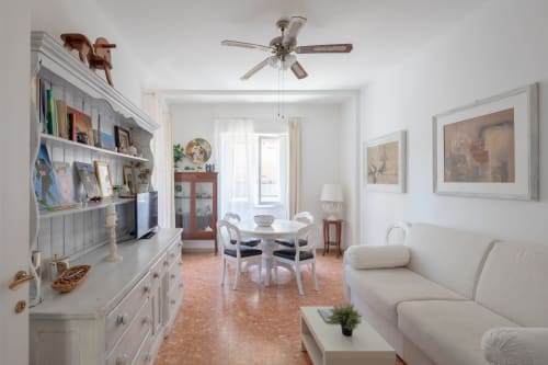 Stella Polare luxury apartment in Ostia: spacious living room with white sofa, dining area, ceiling fan, and framed artwork