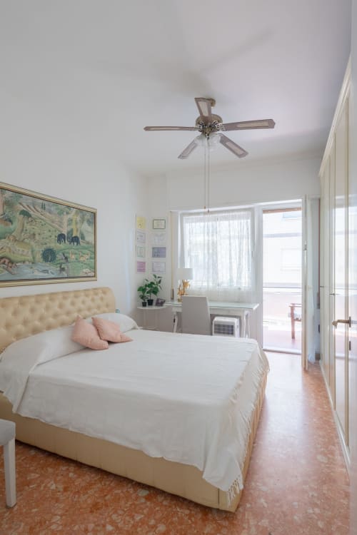 Bright bedroom at Rome Sensorial Rooms in Ostia with cream tufted bed, ceiling fan, and balcony access