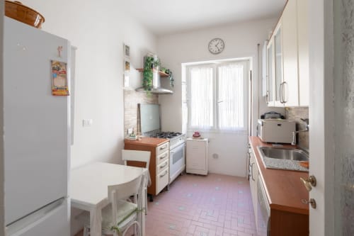 Bright kitchen in Stella Polare Luxury Home, Ostia. White cabinets, terracotta tile floor, dining area with natural light.