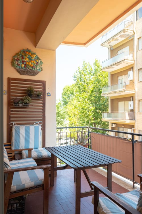 Sunny balcony at Rome Sensorial Rooms in Ostia with striped chairs, wooden table, and city views