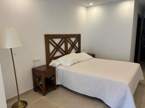 Modern bedroom with wooden X-frame bed and white bedding at Hotel Mulhacén Trevélez, Granada
